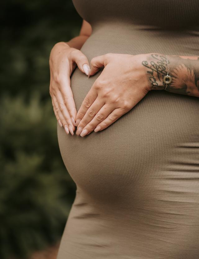 Hände formen ein Herz auf einem Babybauch im grünen Kleid